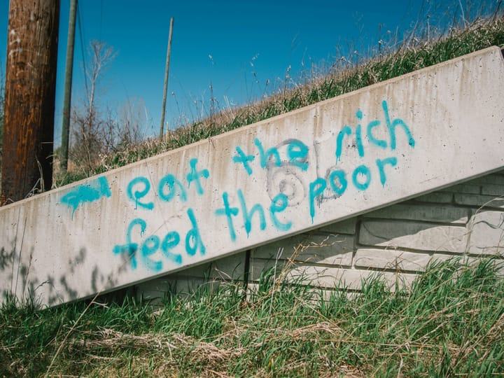 Image shows graffiti on concrete that says "eat the rich, feed the poor"